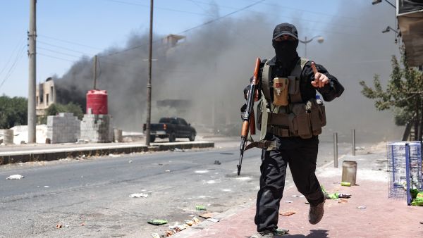 Heavy smoke rises as a member of Bedouin and tribal forces runs during clashes with Druze fighters in Syria's southern city of Sweida, despite an announcement by the Syrian interim president of an "immediate ceasefire" on July 19, 2025. (Photo by OMAR HAJ KADOUR / AFP) Jihadist Omar Omsen